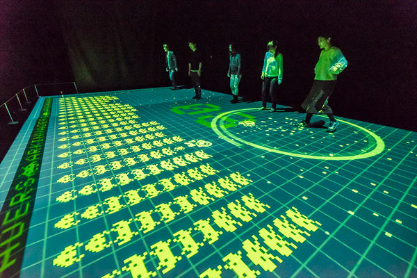 People playing Arkinvaders by kicking glowing projected circles toward Space Invaders on a floor