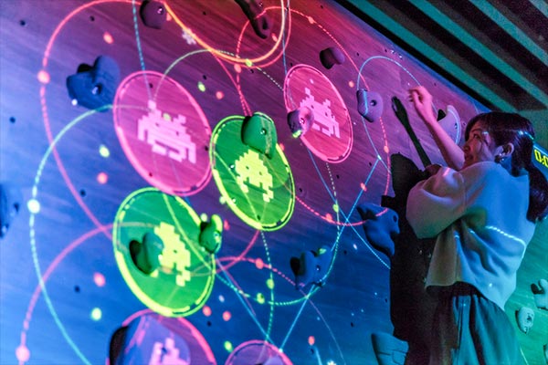 A climber reaching for projected Space Invaders on an indoor bouldering wall